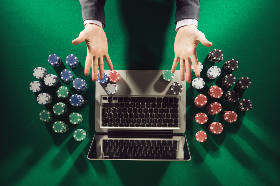 Crypto casino site open on a MacBook, surrounded by poker chips, with two hands reaching out